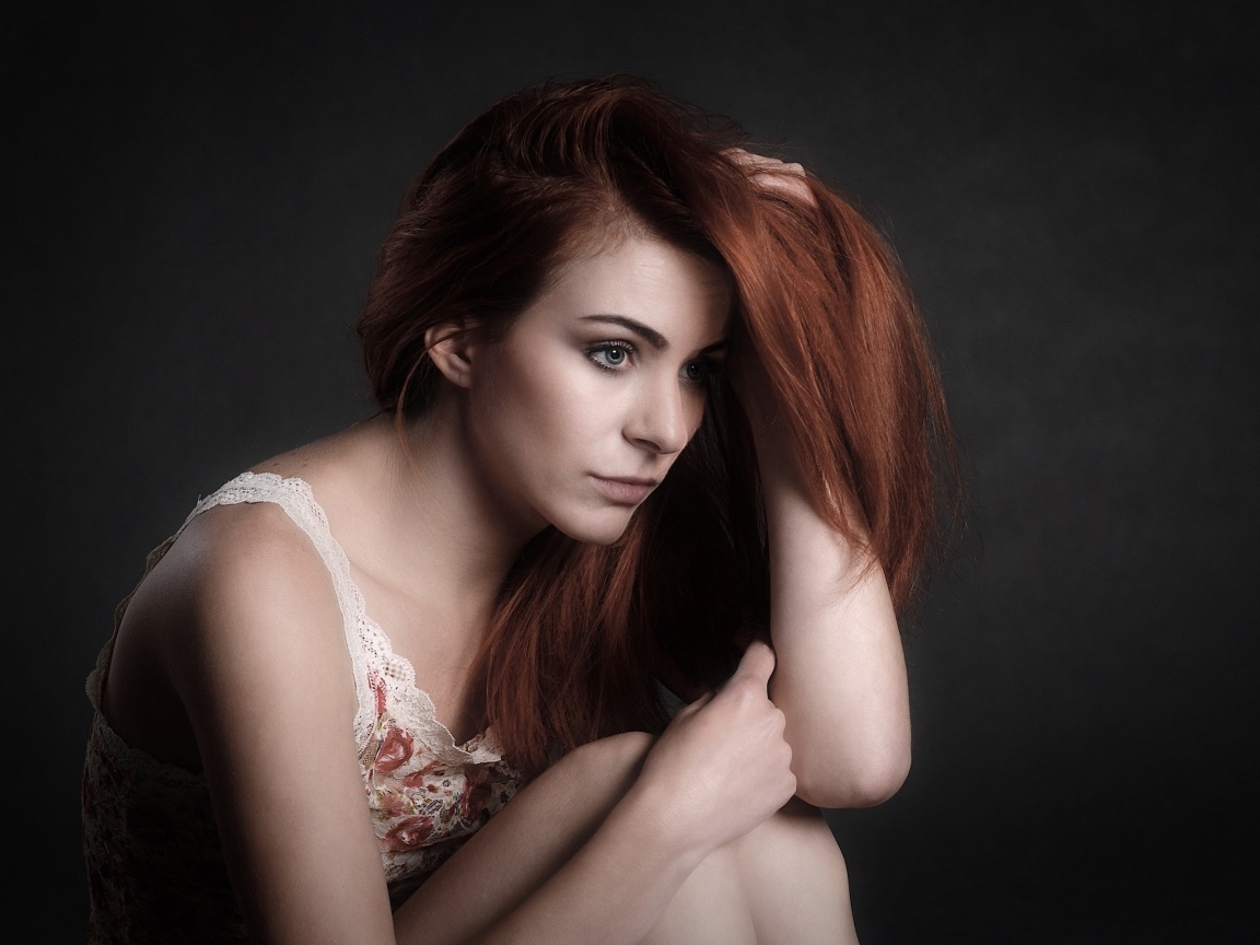 Задумчивая рыжеволосая девушка на сером фоне