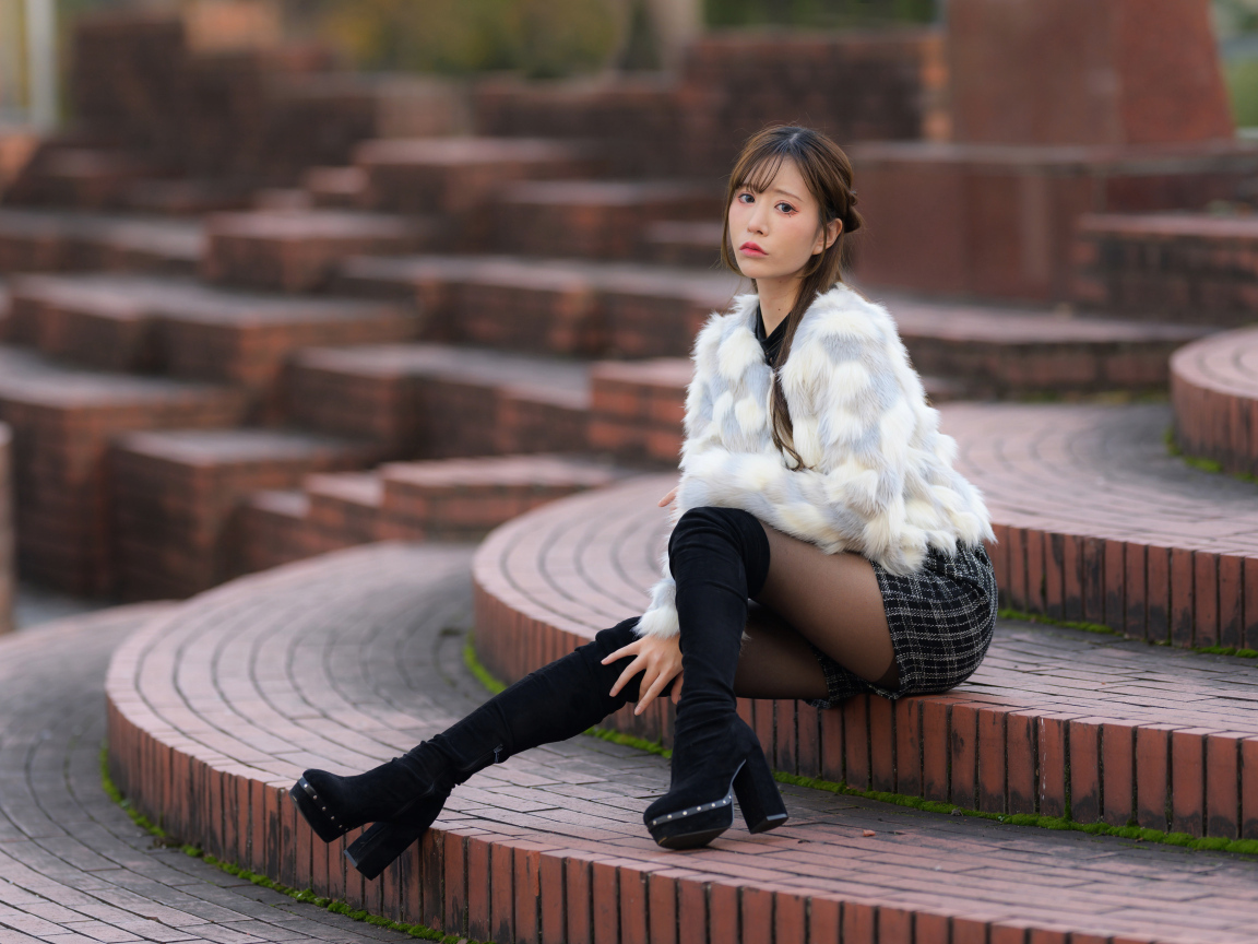 Грустная азиатка в шубе сидит на ступеньках