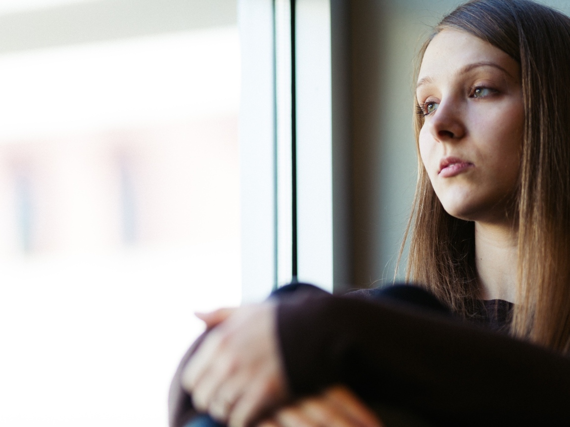Грустная девушка сидит у окна