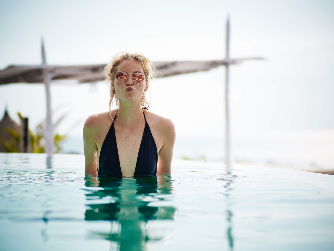 Довольная девушка в очках стоит в бассейне