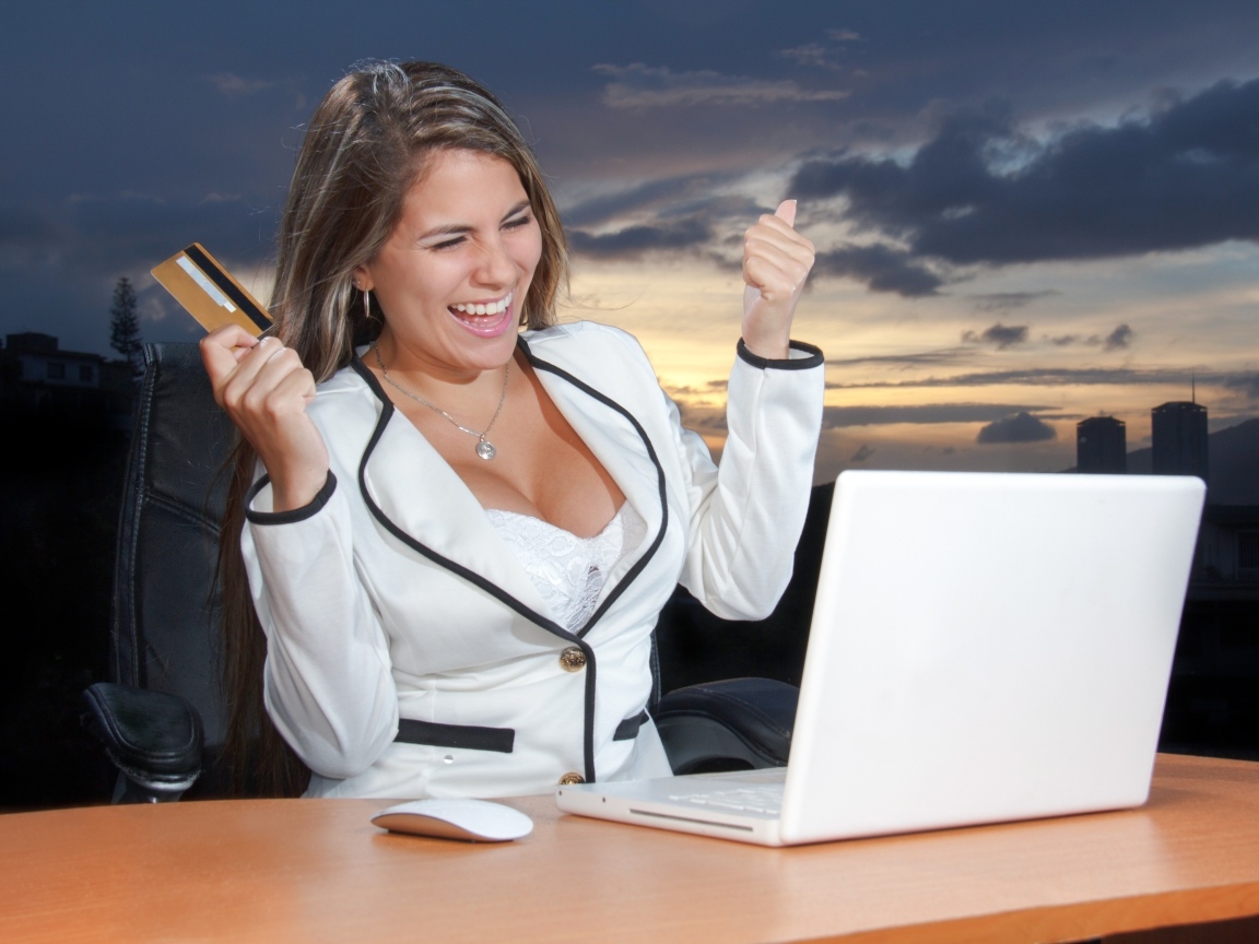 Довольная женщина с карточкой за столом с ноутбуком