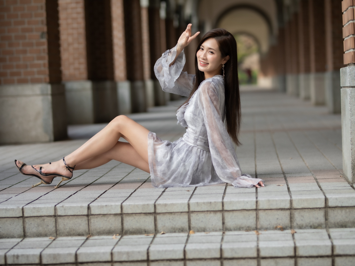 Улыбающаяся девушка азиатка сидит у ступеней