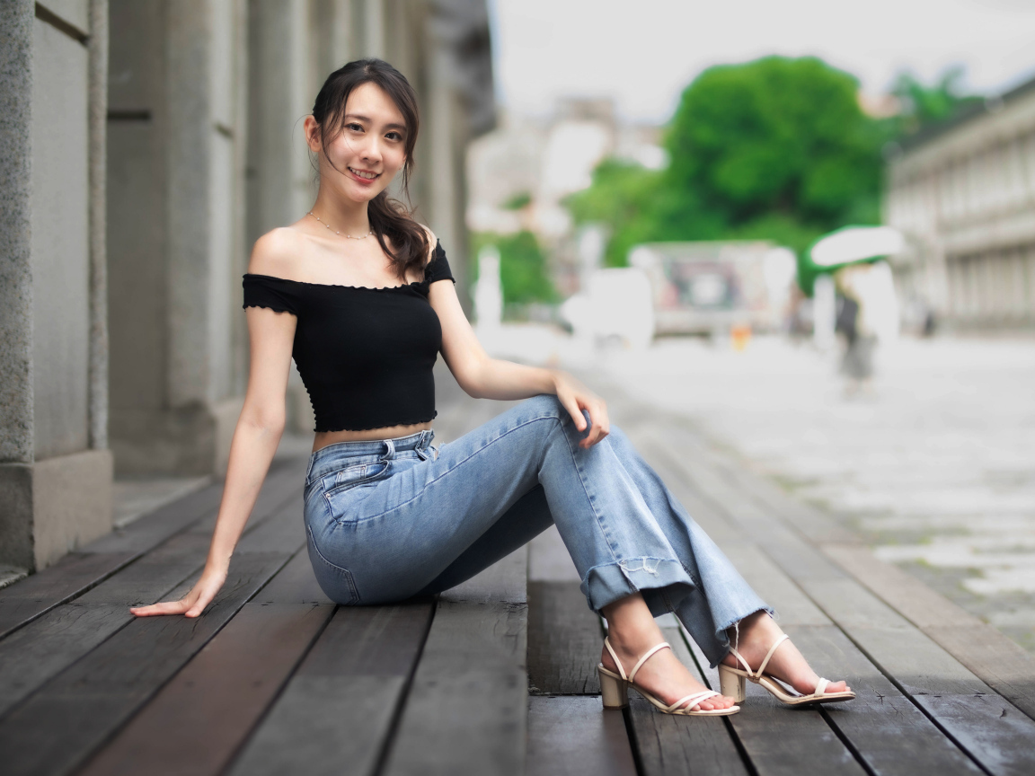 Улыбающаяся азиатка в джинсах сидит на пороге