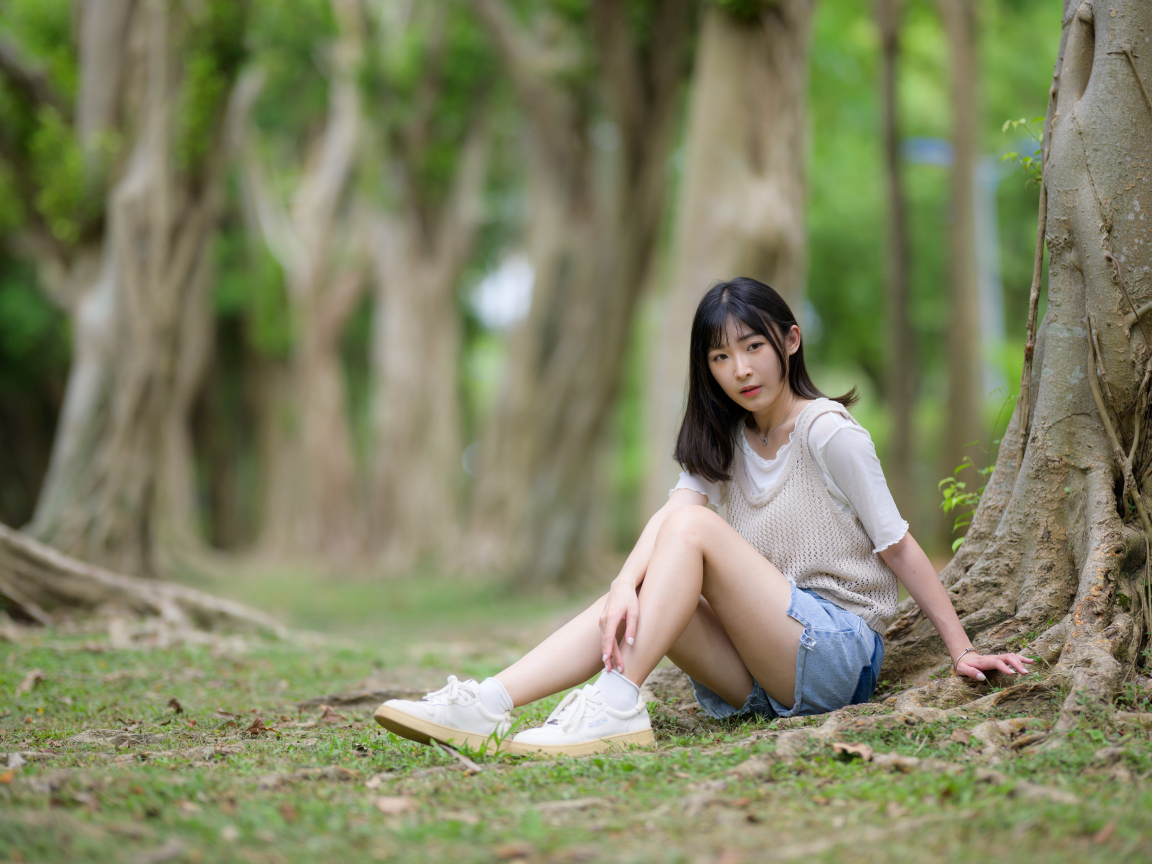 Молодая девушка азиатка сидит у дерева в парке
