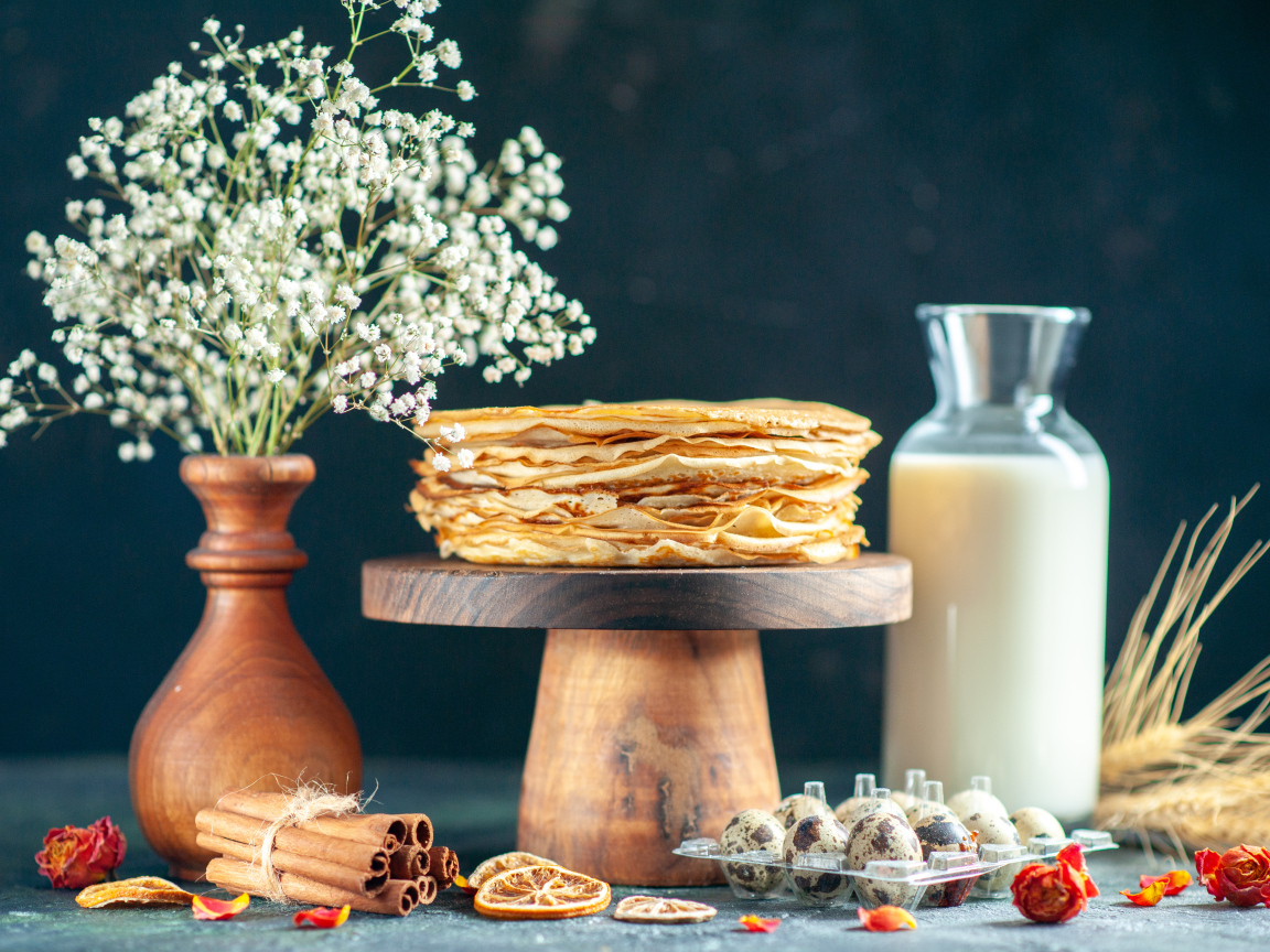 Тонкие блины на столе с молоком, букетом цветов и специями