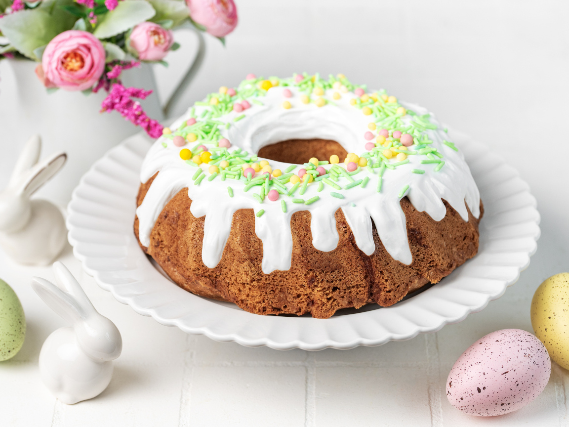Сладкий пасхальный кулич с яйцами и цветами на столе