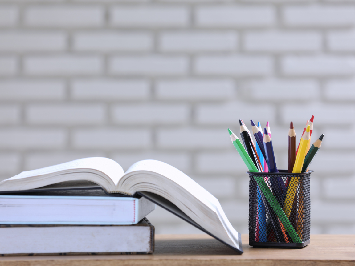 Разноцветные карандаши на столе с книгами 