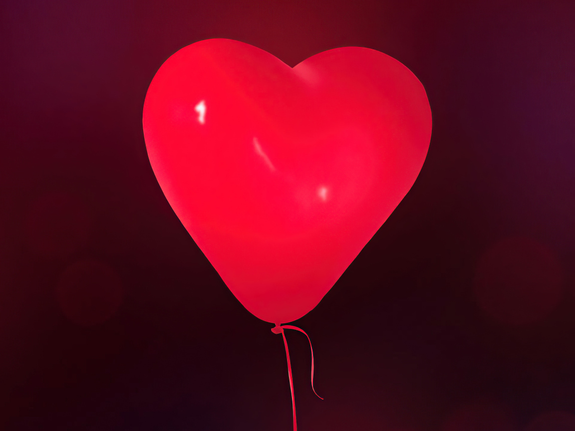 Красный шарик в форме сердца на фоне стены