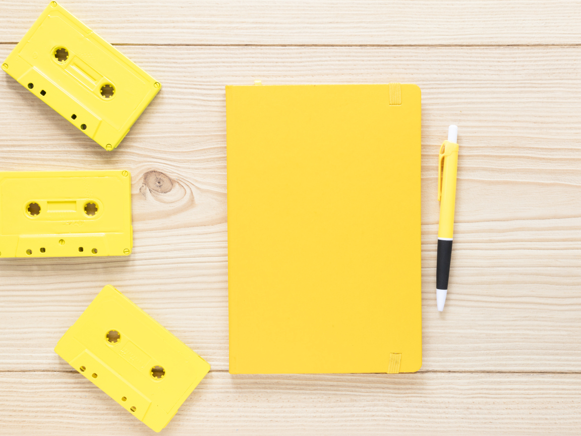Желтый блокнот с ручкой и кассетами на столе