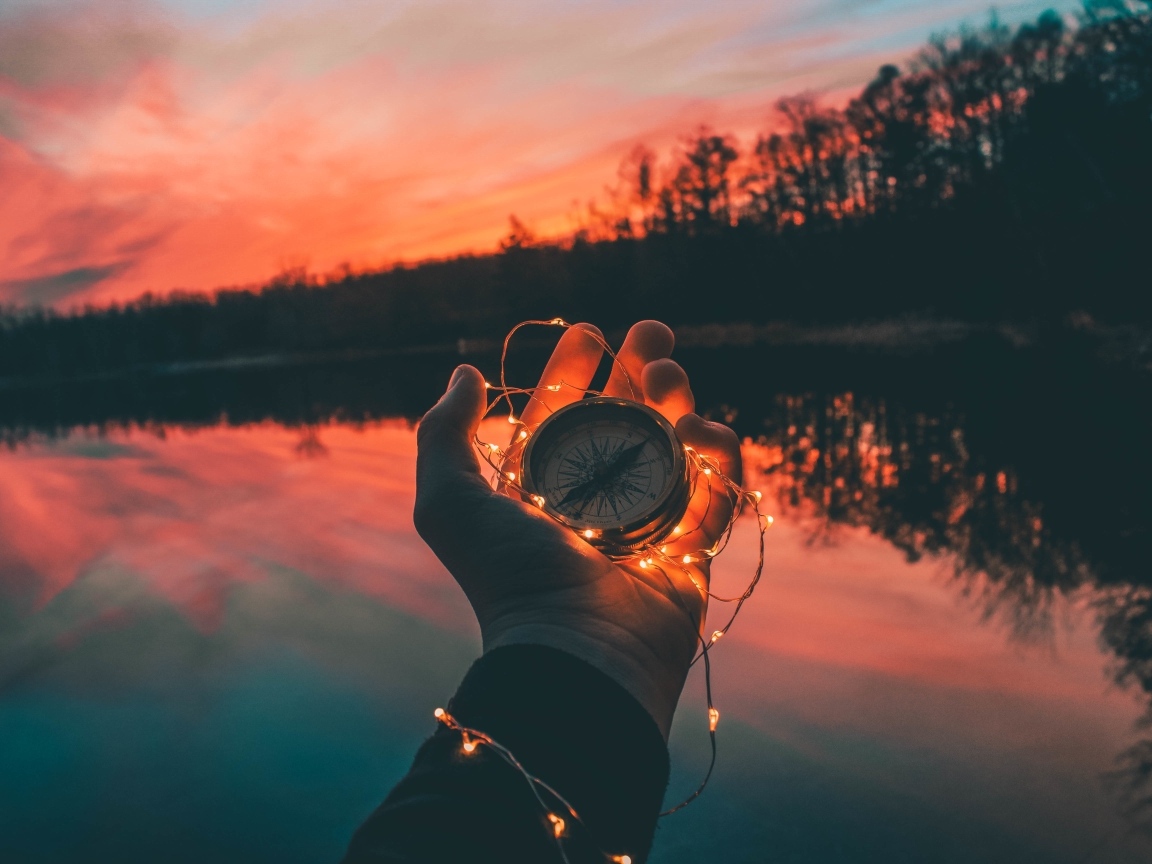 Компас с гирляндой в руке у реки