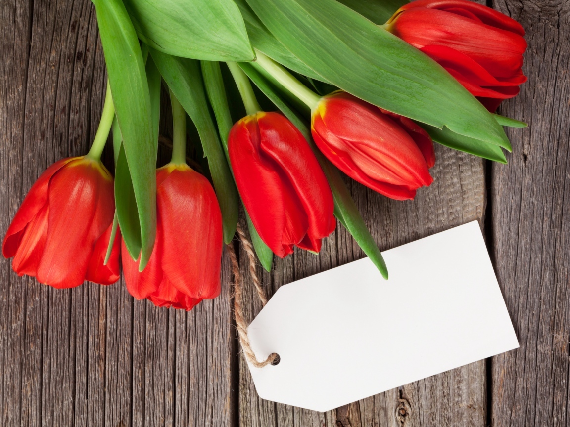 Букет красных тюльпанов с открыткой на деревянном столе