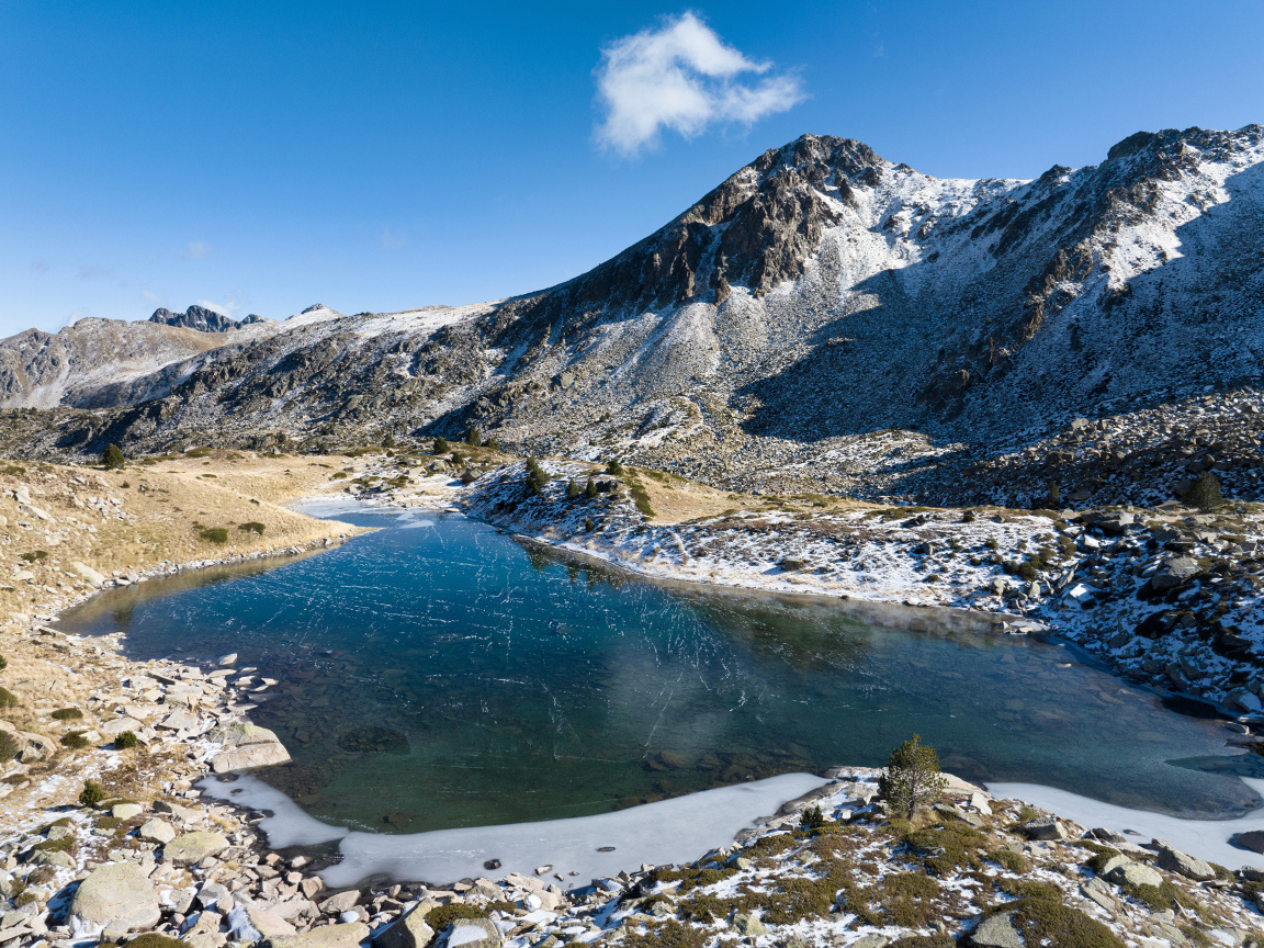 Покрытое льдом озеро в заснеженных горах в лучах солнца, Андорра