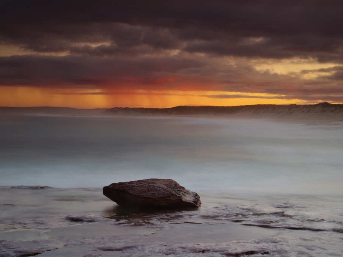 Большой камень в воде на фоне грозового неба в море