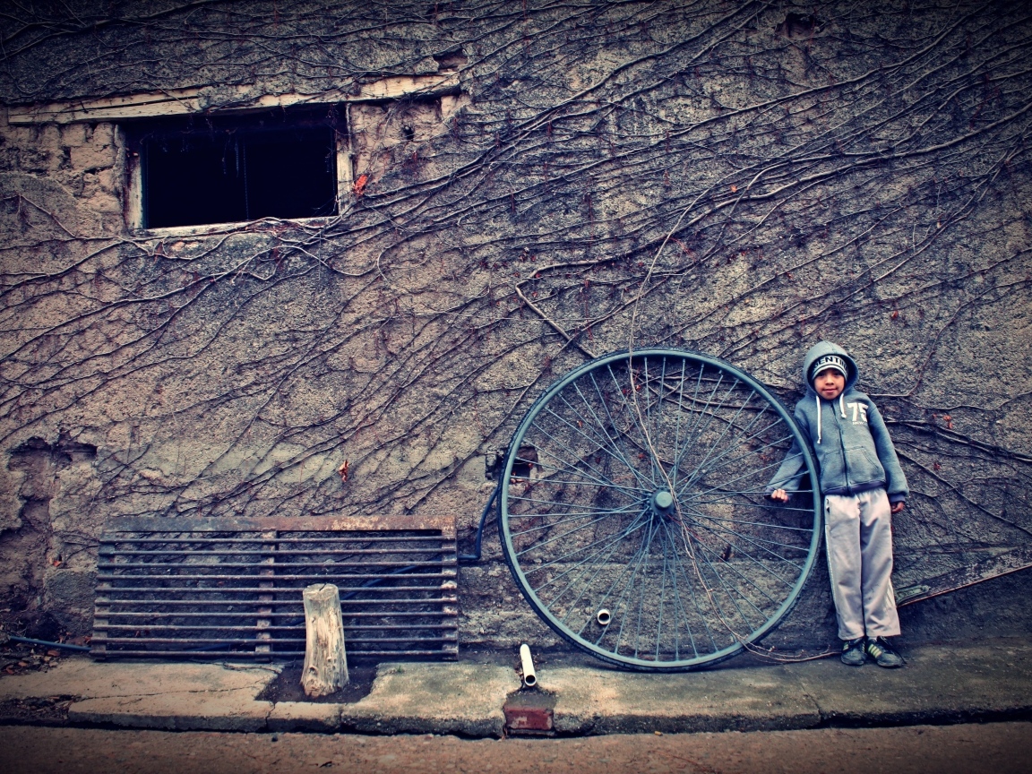 Мальчик с большим колесом стоит у стены