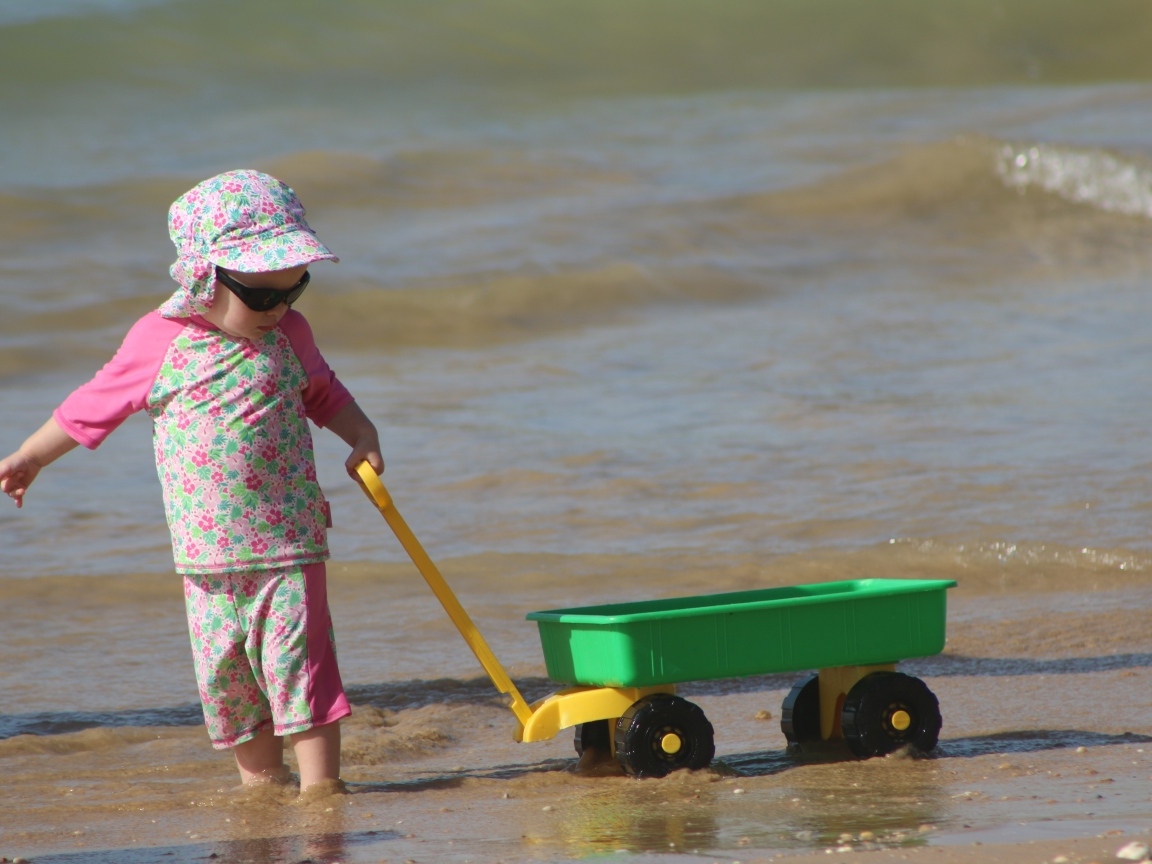 Девочка с машинкой играет на песке у моря