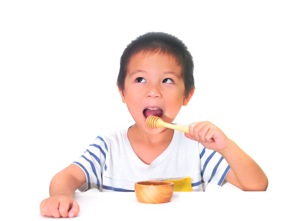 Мальчик азиат ест мед на сером фоне