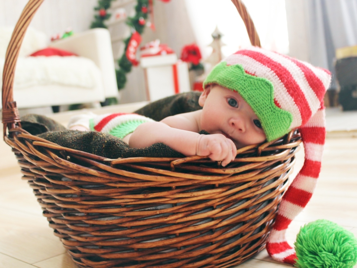 Милый малыш в большой вязаной шапке в корзине