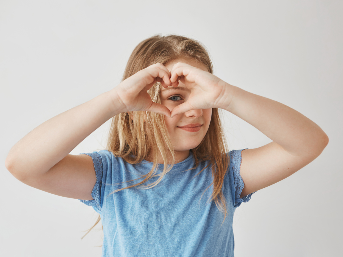 Девочка делает сердечко руками на сером фоне