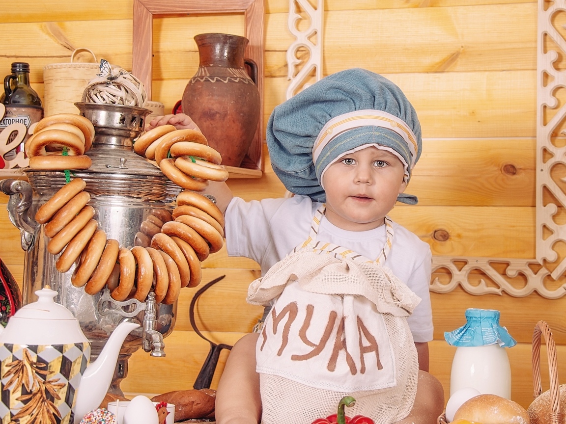 Маленький мальчик повар с продуктами и самоваром на столе