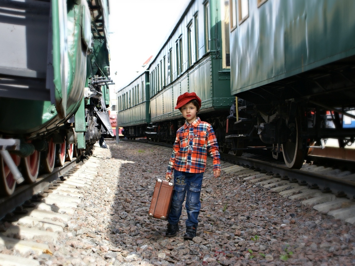 Маленький мальчик с чемоданом у вагонов