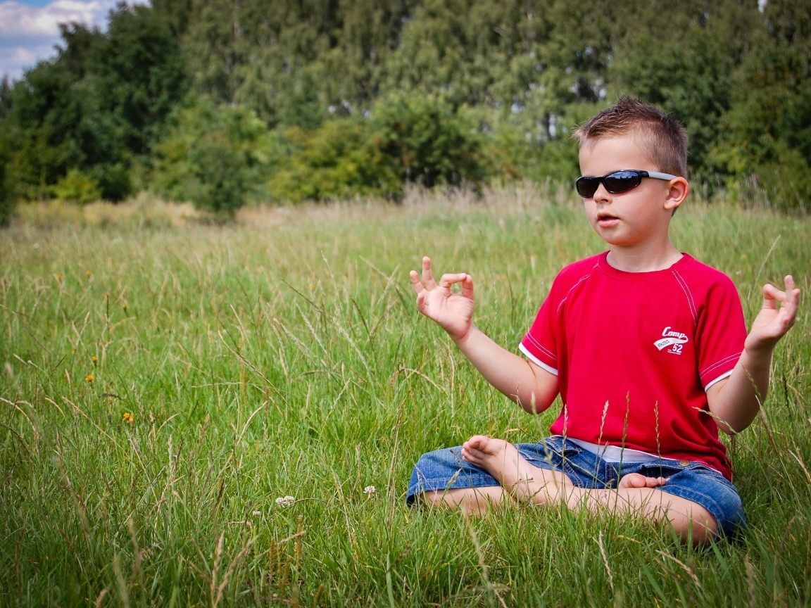 Маленький мальчик в очках медитирует на зеленой траве