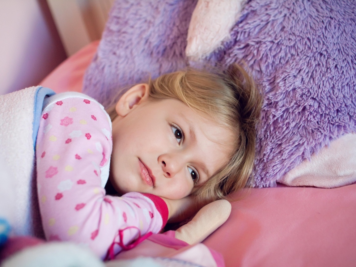 Маленькая кареглазая девочка лежит в кровати 