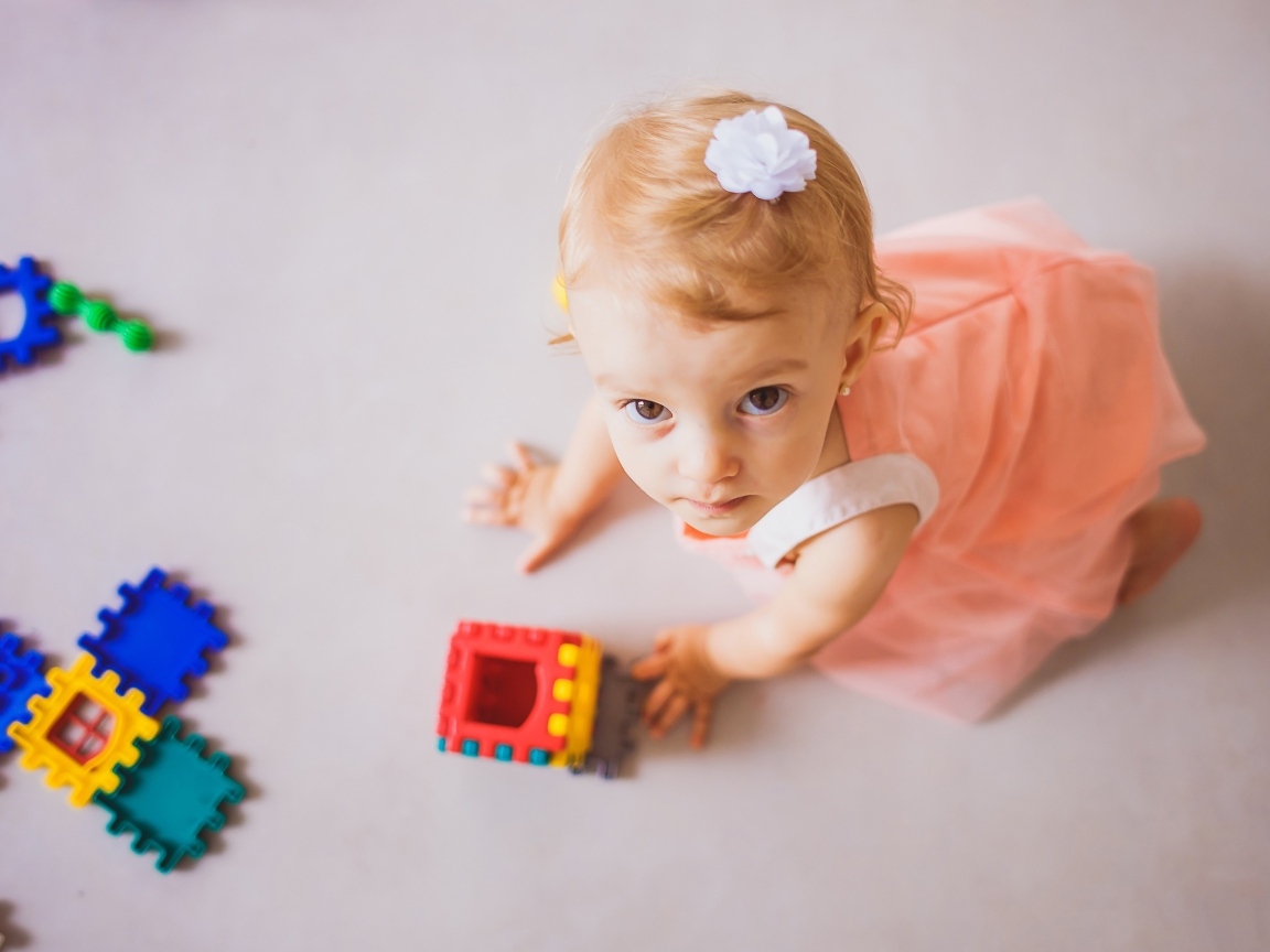 Маленькая девочка играет на полу с конструктором