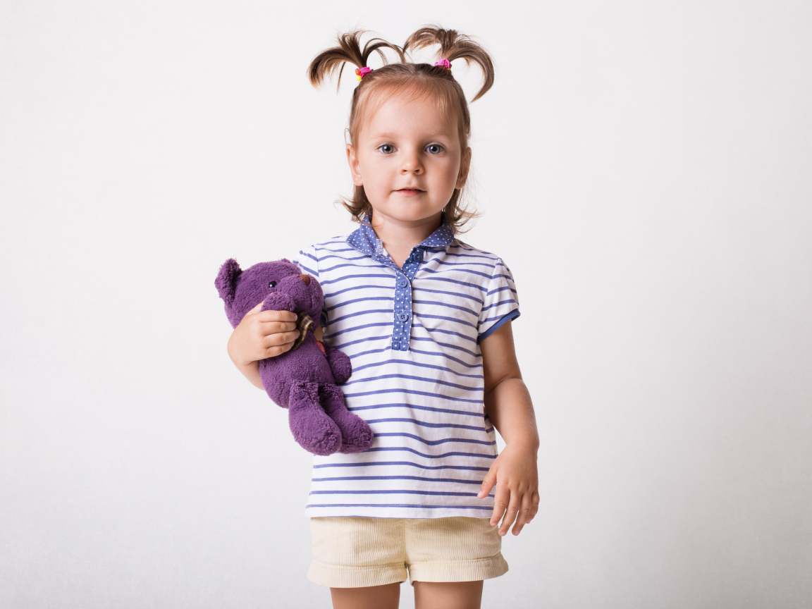 Маленькая девочка с игрушечным медведем на сером фоне