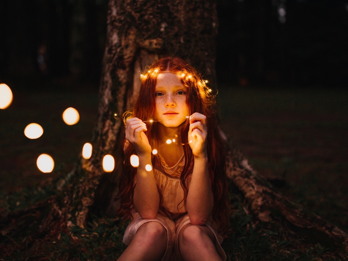 Рыжеволосая девочка с гирляндой под деревом