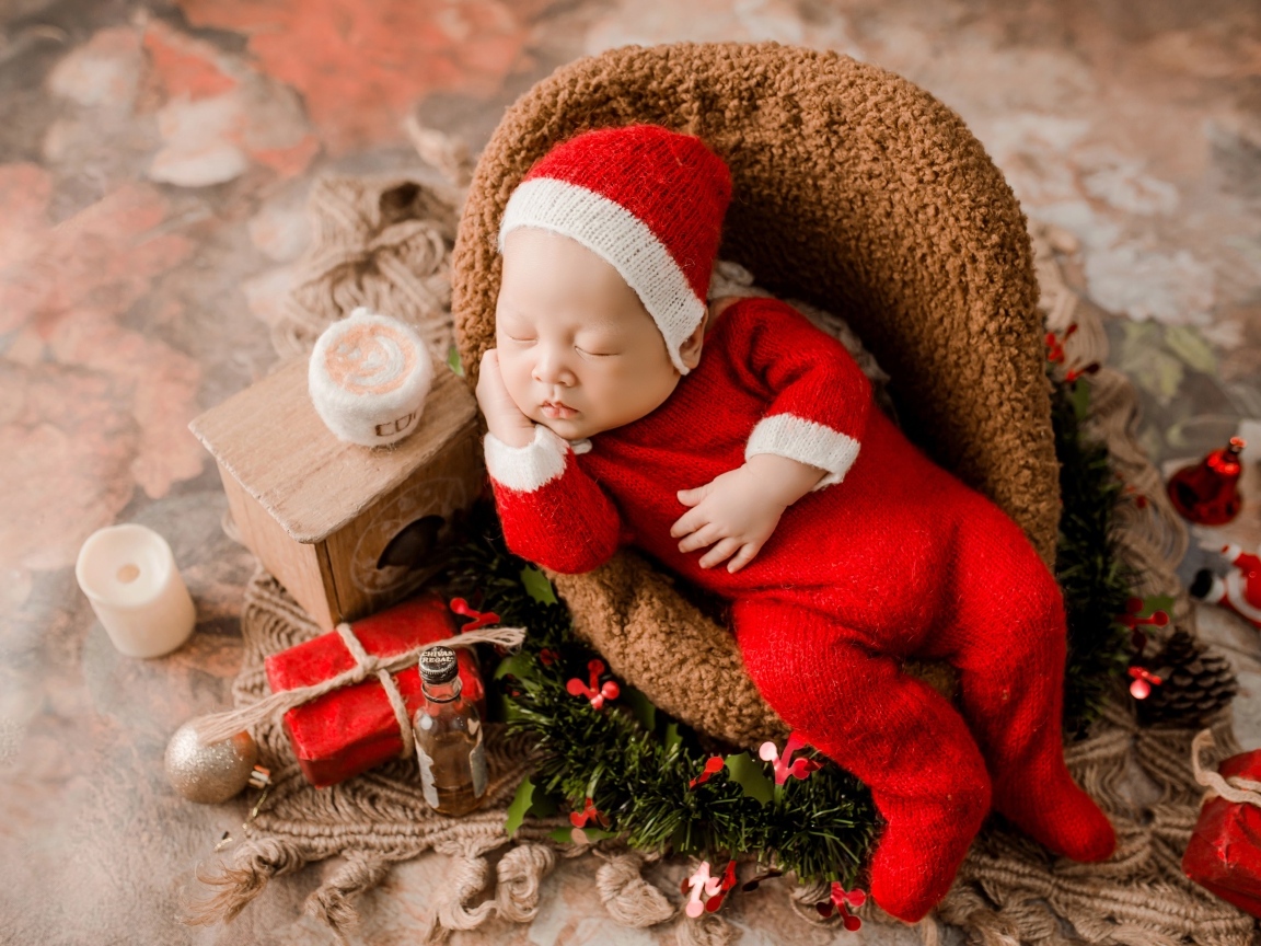 Спящий новорожденный ребенок в красном новогоднем костюме