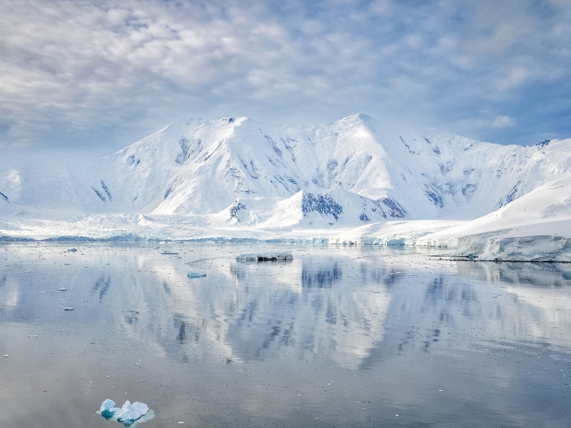 Заснеженные горы под белыми облаками у океана, Антарктида 