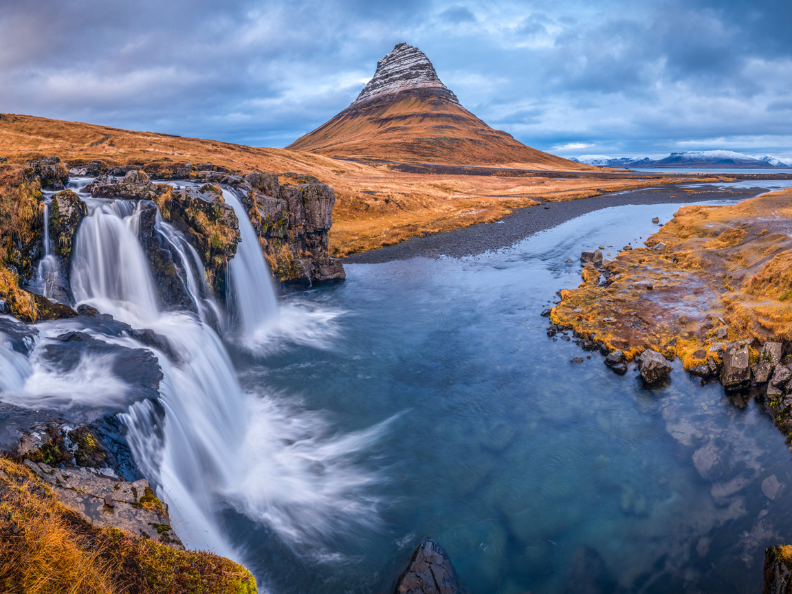 Вид на реку, водопад и гору Киркьюфетль под пасмурным небом Исладнии