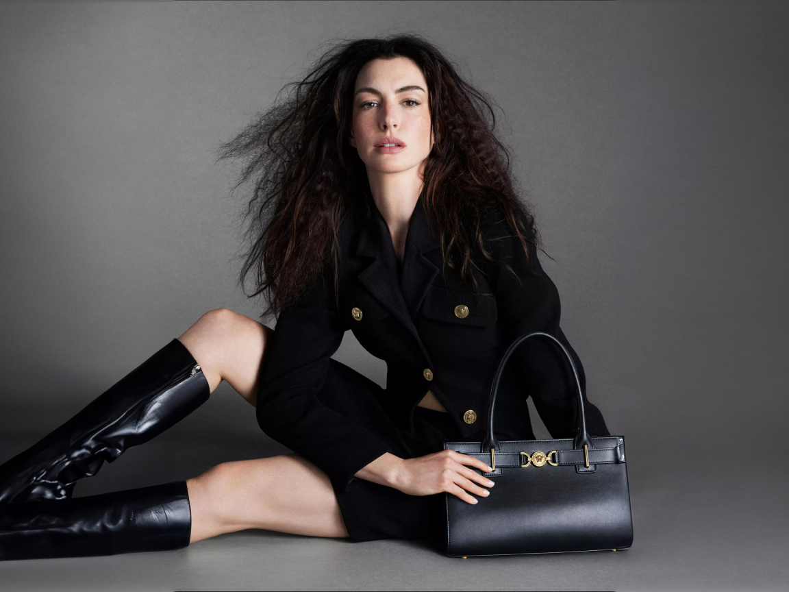 Актриса Энн Хэтэуэй в черных сапогах с сумочкой на сером фоне