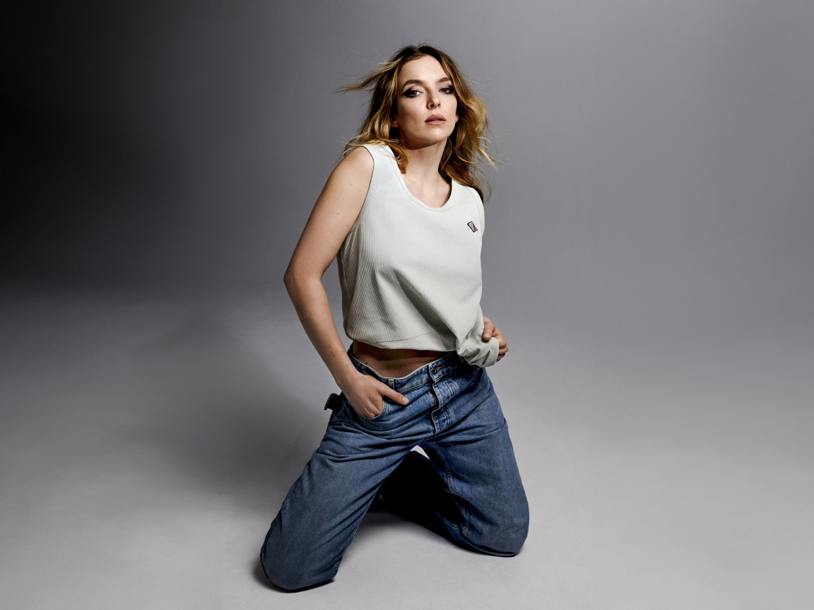 Британская актриса Джоди Комер в джинсах на сером фоне