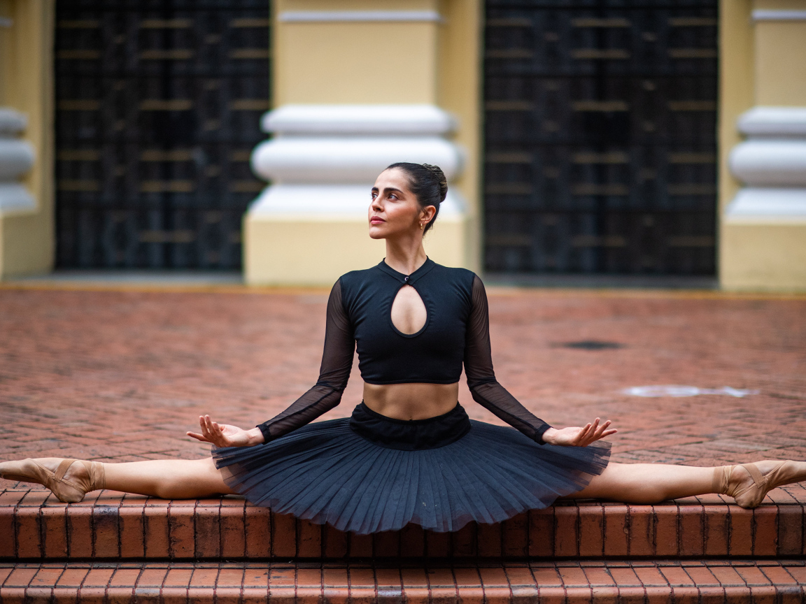 Девушка балерина в черном сидит на шпагате