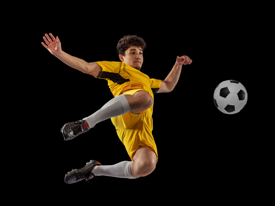 Мужчина футболист отбивает мяч на черном фоне
