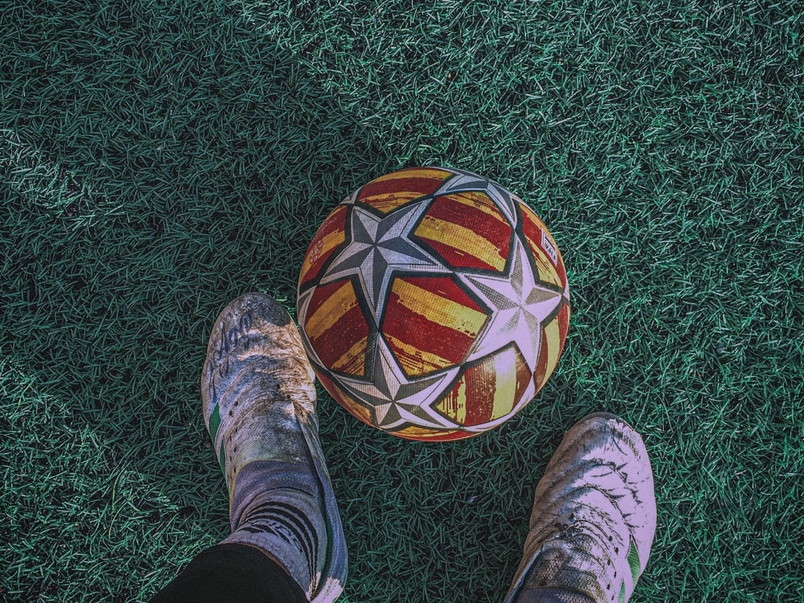 Футбольный мяч на зеленом поле с ногами футболиста
