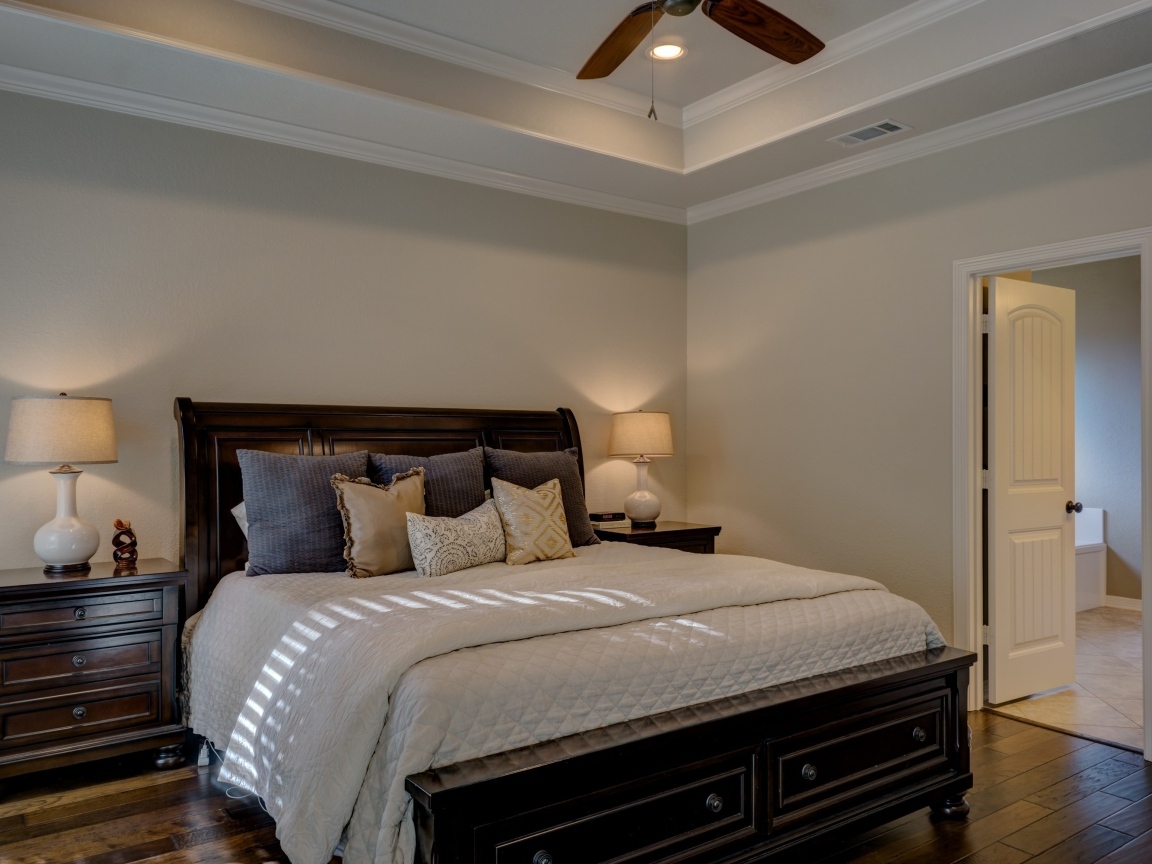 Деревянная кровать с белым покрывалом и подушками в спальне