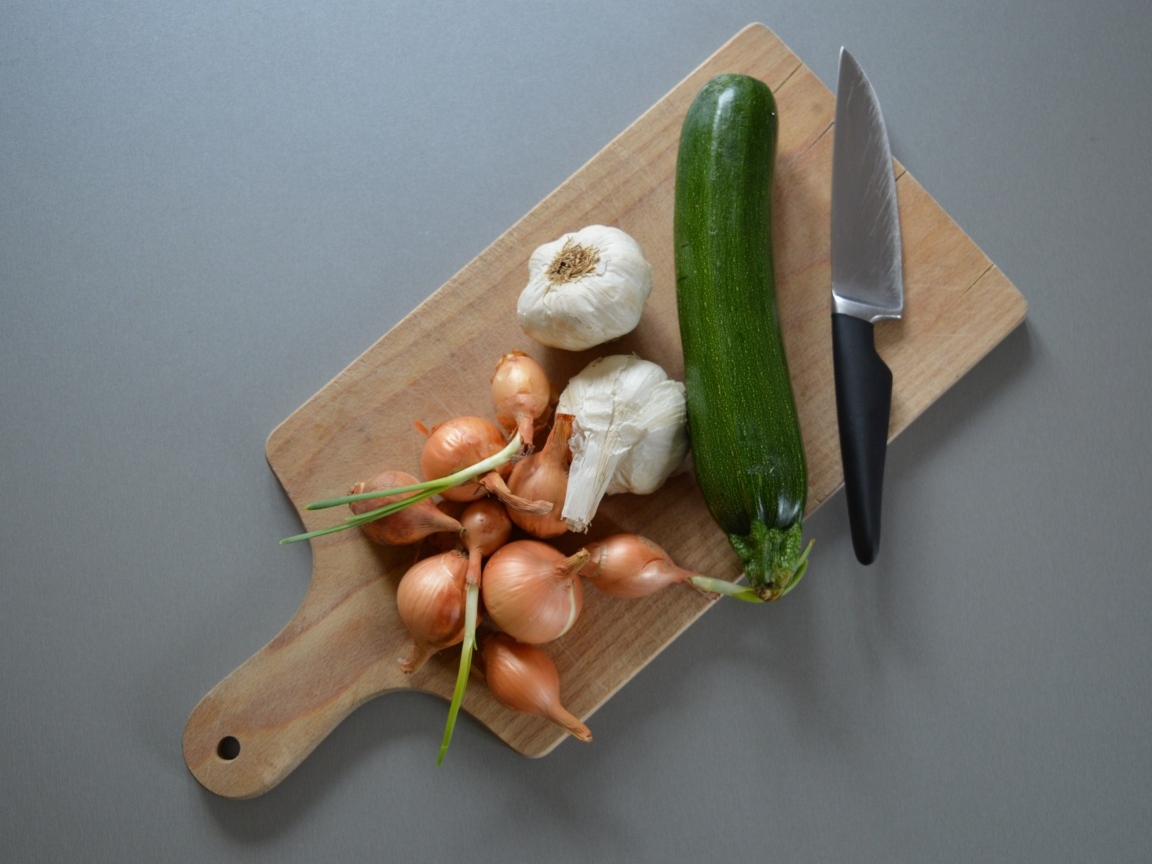 Лук, чеснок и кабачок на разделочной доске с ножом
