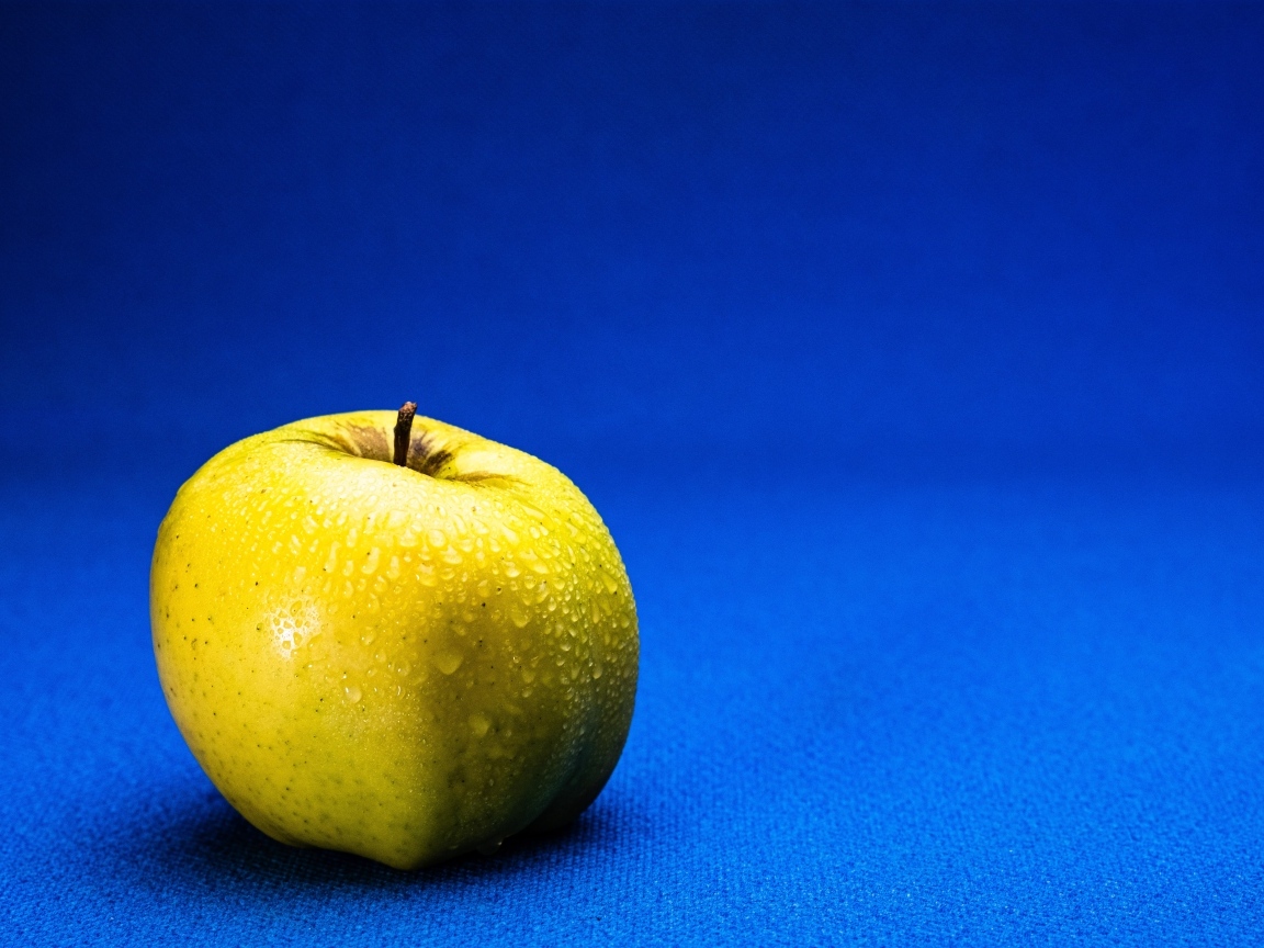 Большое желтое мокрое яблоко на синем фоне