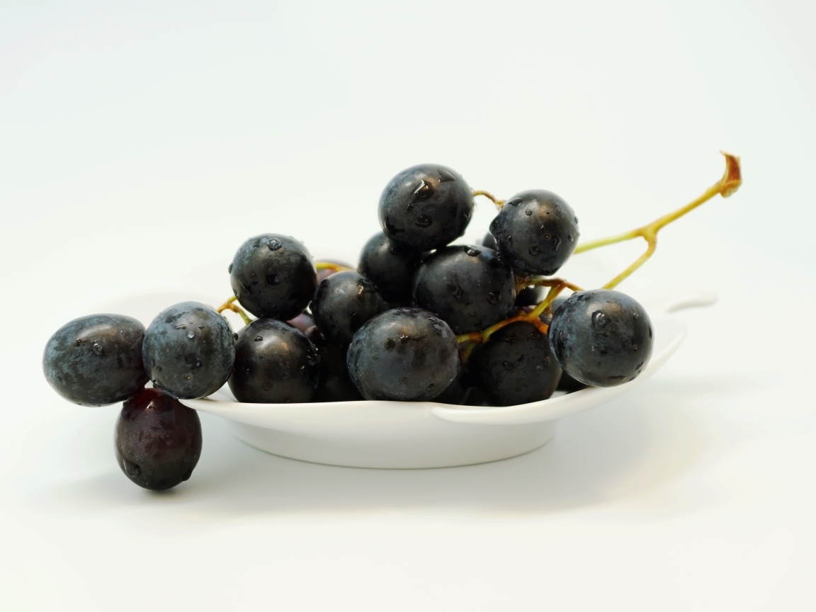 Гроздь синего винограда в тарелке на белом фоне