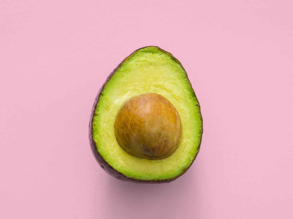 Половина авокадо с большой косточкой на розовом фоне