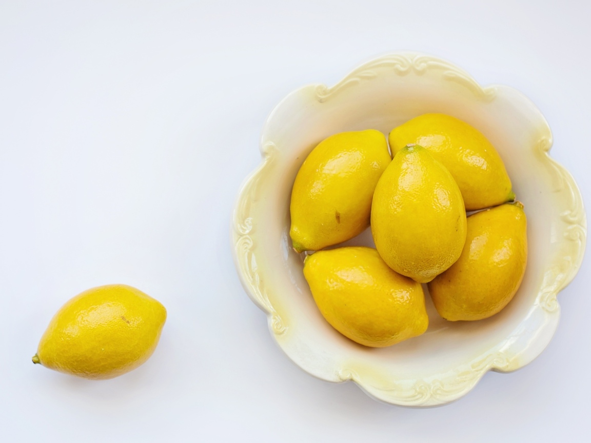 Много желтых лимонов в тарелке на сером фоне