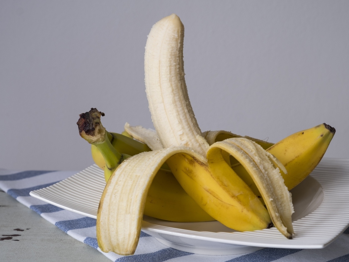Очищенный банан на тарелке на сером фоне