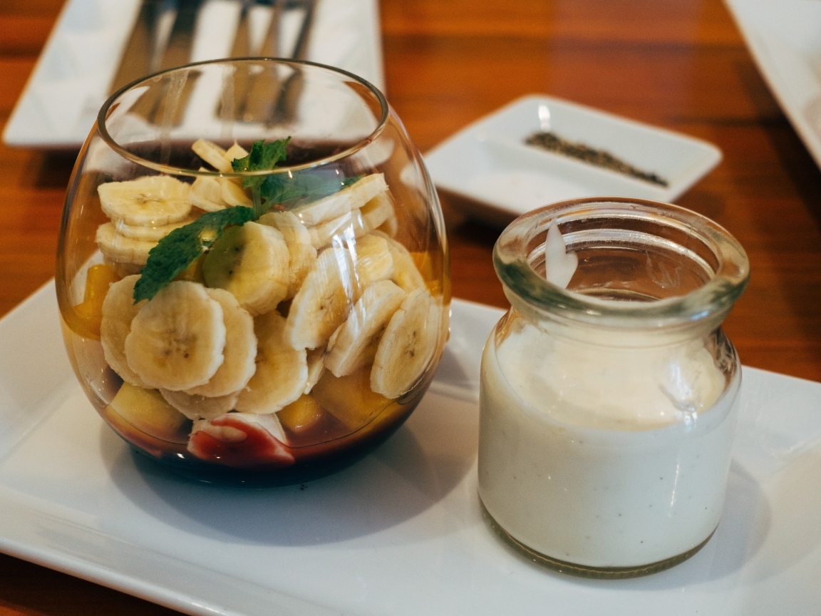 Нарезанные бананы в стакане на столе с йогуртом