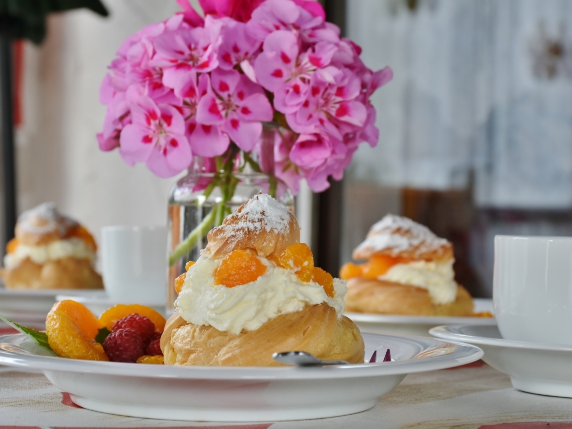 Булочки с кремом и фруктами на столе с букетом