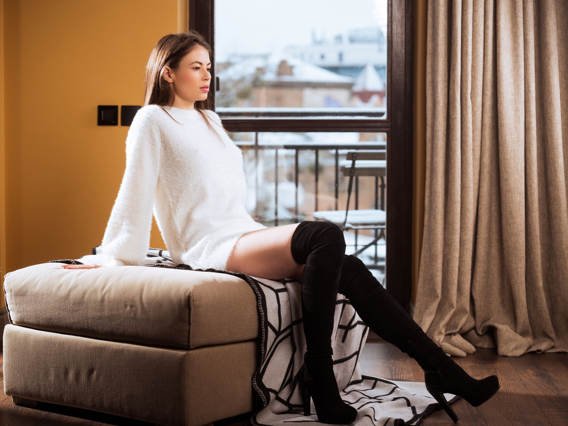 Девушка сидит на кресле в комнате у окна