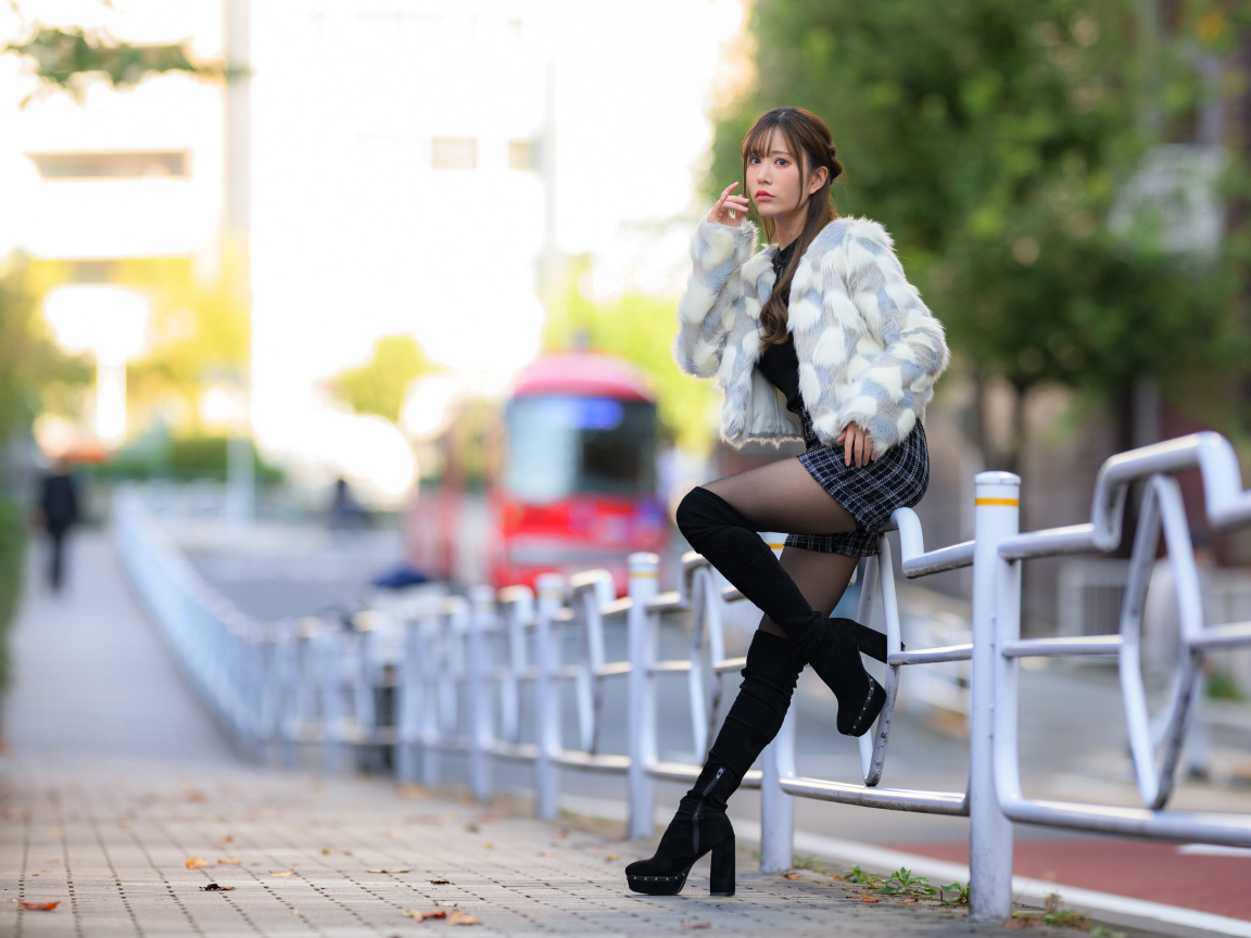 Азиатка в шубе стоит у забора