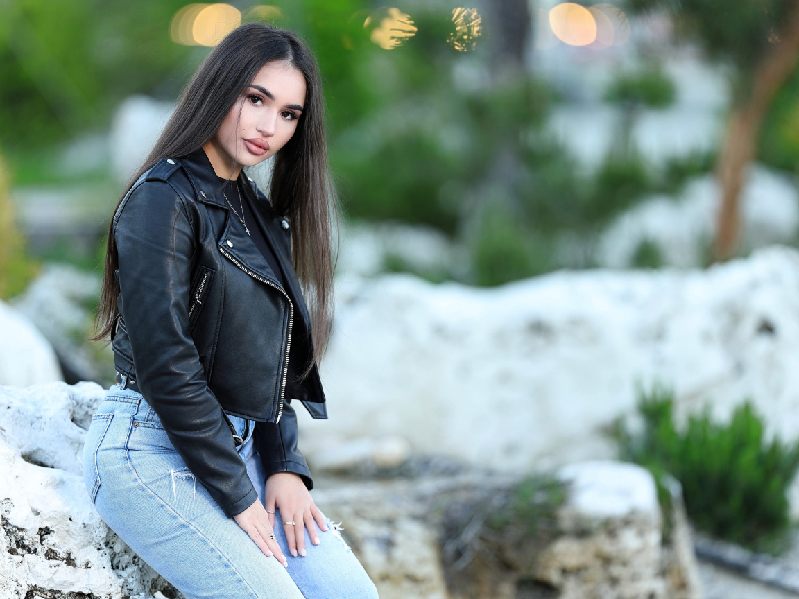 Брюнетка в черной кожаной куртке сидит на камне