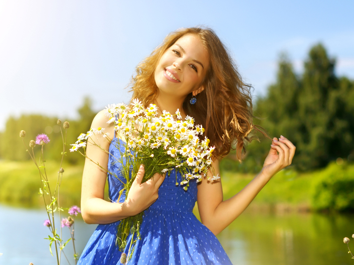 Милая улыбающаяся девушка с букетом ромашек у пруда летом